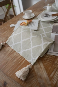 Detail of sage green table runner featuring Moroccan geometric patterns and white tassels