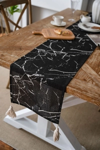 Detail of black marble print table runner featuring cream tassels on a dark wood table