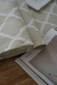 Close-up of sage green linen table runner with white geometric quatrefoil pattern