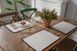 Set of 4 beige cotton linen placemats with black wavy embroidered edges on wooden table