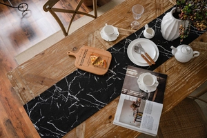 Detail of long black table runner with white marble pattern on a wooden dining table