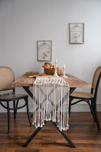 Detail of bohemian hand-woven cotton table runner with long tassels on a wooden table