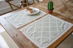 Detailed view of sage green table placemats with white clover pattern and lace borders