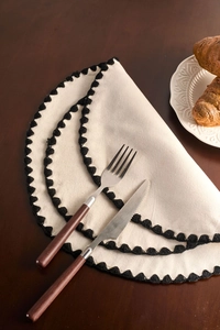 Close-up of beige cotton linen placemat with black crochet wavy edge on wooden table