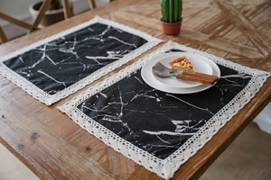 Close-up of black marble print table mat with delicate white lace trim on wooden table