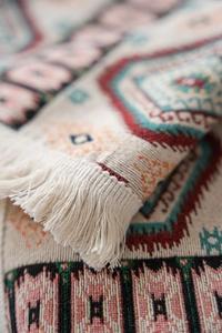 Detailed close-up of colorful geometric woven fabric with handmade off-white fringe tassels