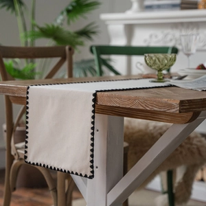 Minimalist beige table runner with black scalloped embroidery on a rustic wooden dining table