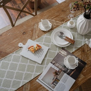 Light green cotton linen table runner with white Moroccan geometric patterns on wood