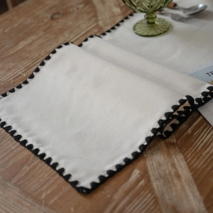 Minimalist beige embroidered table runner with black scalloped edges on wooden table