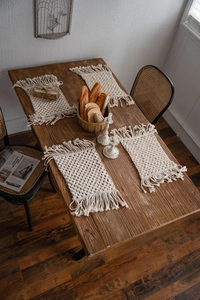 Set of four handmade macrame placemats with fringe on a rustic wooden dining table