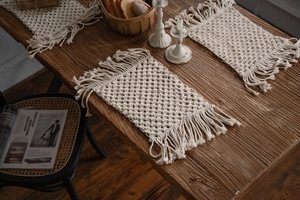 Detail of off-white handmade macrame placemat with fringe edges on a wooden table