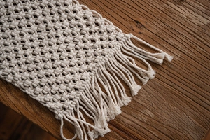 Detail of cream macrame table runner with handmade hollow weaving and long fringe tassels