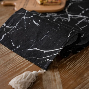 Black table runner with white marble print and cream tassels on a wooden tabletop