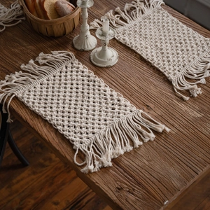 Set of two bohemian hand-woven cream cotton placemats with fringe on a dark wooden table