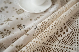Detailed close-up of pastoral linen tablecloth with floral print and crochet lace edge
