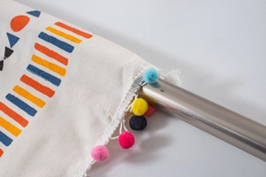 Detail of canvas curtain with geometric prints and colorful pom-poms on metal rod