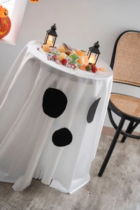 Detail of white Halloween round tablecloth featuring black ghost faces and drape effect