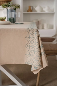 Detailed close-up of blue geometric embroidery on beige cotton linen tablecloth