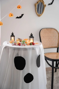 Detail of white Halloween ghost tablecloth with black felt face on round dinner table