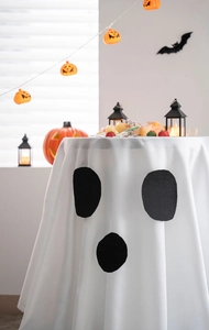 Close-up of white Halloween ghost tablecloth with black face print and spooky party decor