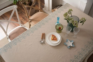 Detail of beige cotton linen tablecloth with blue geometric embroidery in a cozy dining setting