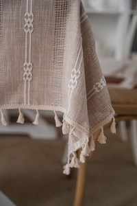 Detail of coffee brown striped tablecloth with white floral embroidery and tassels