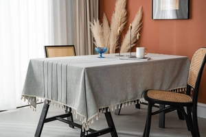 Detail of light gray rectangular tablecloth featuring elegant stripes and cream tassels