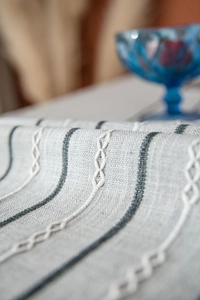 Macro view of grey linen tablecloth featuring striped texture and white embroidery detail