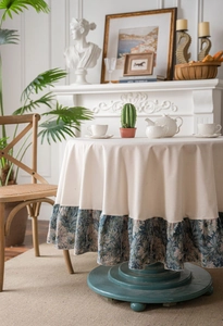 Detail of round beige tablecloth featuring vintage blue floral ruffled hem and elegant texture