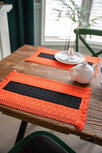 Close-up of orange crochet table runner with black geometric pattern and fringe details