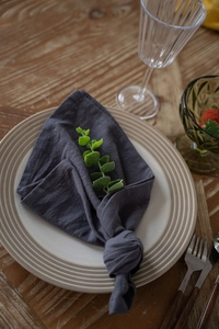 Close-up of knotted charcoal grey cotton napkin on ceramic plate with green leaf detail