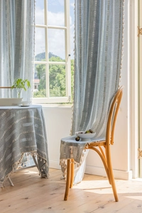 Detail of light blue curtains featuring white geometric patterns and small fringe tassel trim