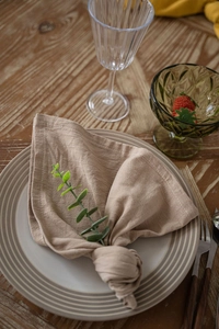 Detail of coffee-colored cotton napkin tied on a plate with eucalyptus leaf decor