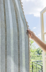 Detail of grey-blue striped semi-sheer linen curtain with ethnic texture and tassels