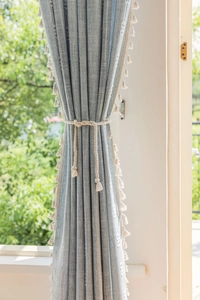 Close-up of textured blue linen curtain with cream pom-pom trim and cotton rope tieback