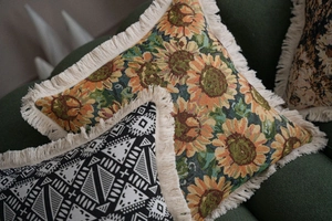Detail of sunflower and geometric jacquard pillows with cream fringe on green sofa