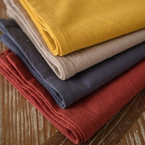 High-quality stacked plain washed cotton napkins in various earthy tones on wooden table