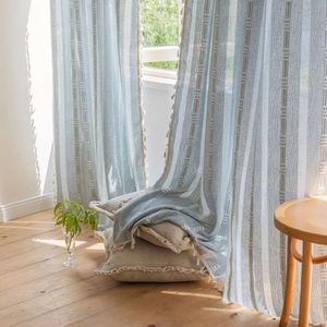 Light blue striped curtains with tassels and matching cushion in natural sunlit room