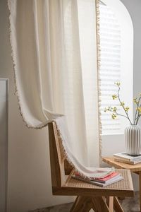 Close-up of cream waffle-weave cotton curtain with elegant fringe tassels in soft lighting