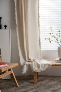 Detail view of cream waffle weave curtain fabric with tassel fringe on a wooden bench