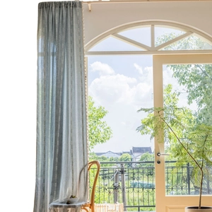 Light blue-grey striped linen curtains with delicate pom-poms in a bright sunny room