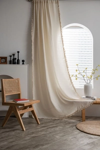 Detail of cream waffle fabric curtain with decorative tassel fringe edges in a home setting