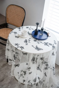 Detail of white mesh lace tablecloth with black butterfly floral embroidery on round table