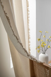 Detail of cream waffle texture curtain with decorative tassel trim in natural sunlight