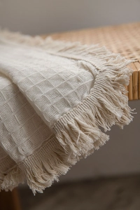 Detail of beige waffle weave fabric with textured tassels on a rustic bench