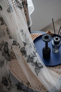 Detailed view of cream lace fabric with intricate black butterfly and flower embroidery