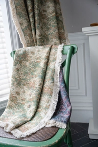 Detail of floral woven throw with fringes on green chair in American country style