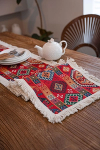 Macro detail of geometric jacquard table runner with white tassels on wood table