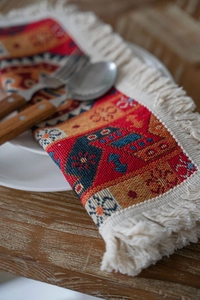 Detail view of woven geometric table runner with red tassels on a wooden surface
