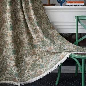 Vintage green floral woven throw blanket with white tassels on a rustic chair